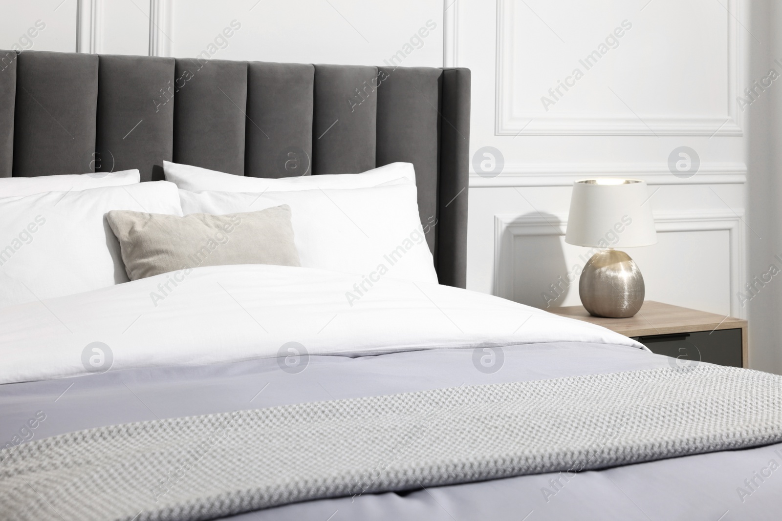 Photo of Comfortable bed near bedside table with lamp in stylish bedroom