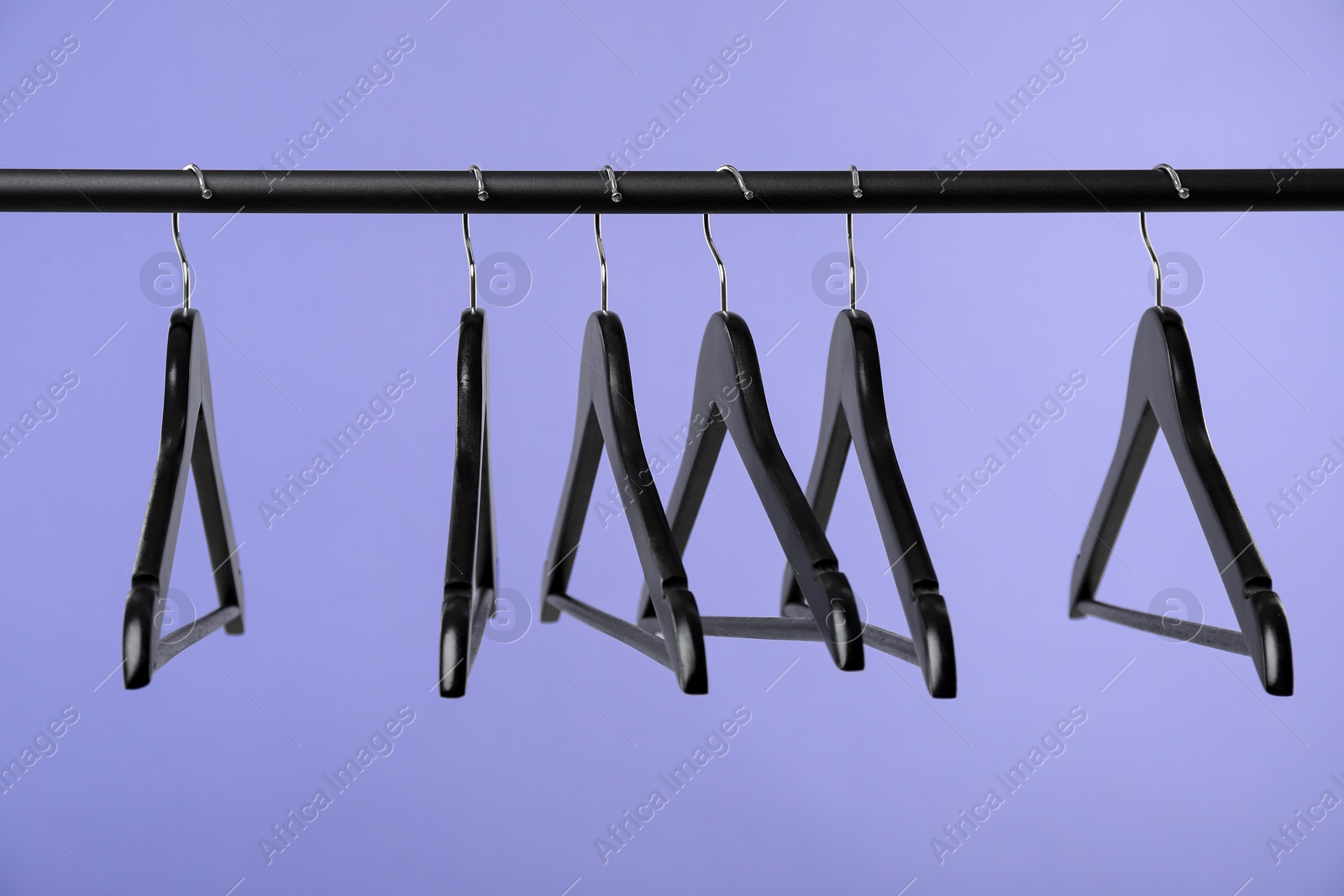 Photo of Black clothes hangers on rack against purple background