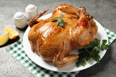 Photo of Tasty roasted chicken with parsley and lemon on grey textured table