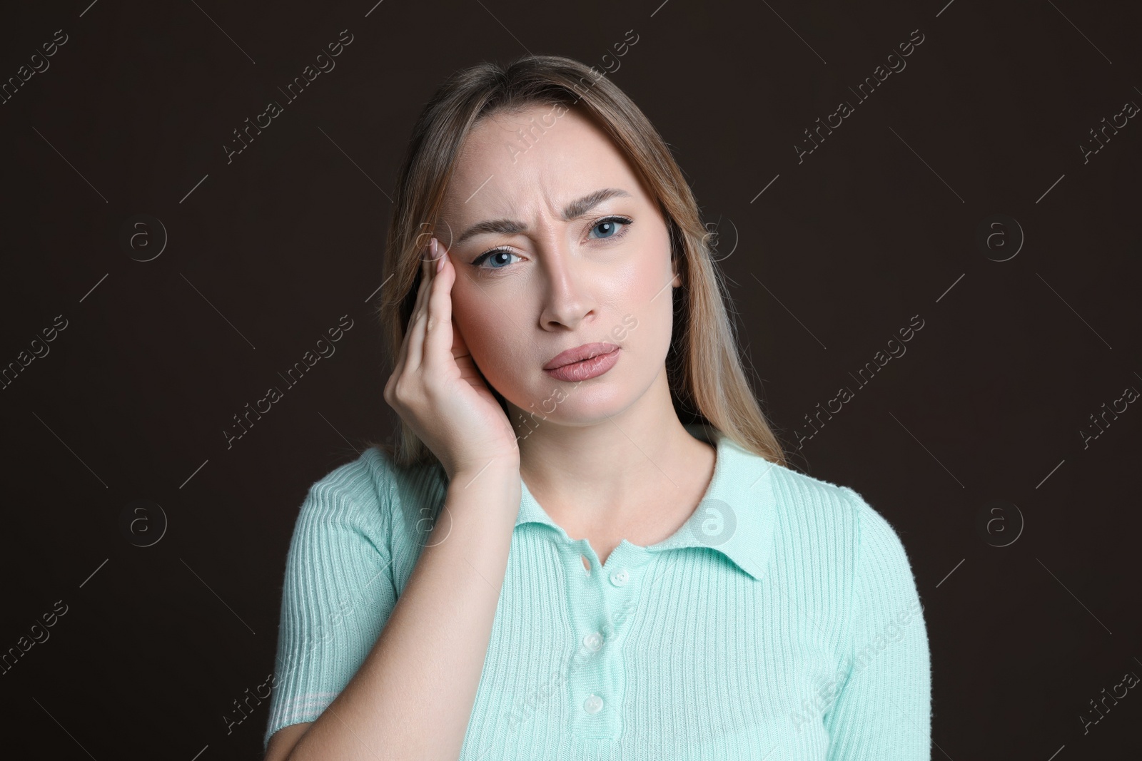 Photo of Young woman suffering from headache on dark brown background
