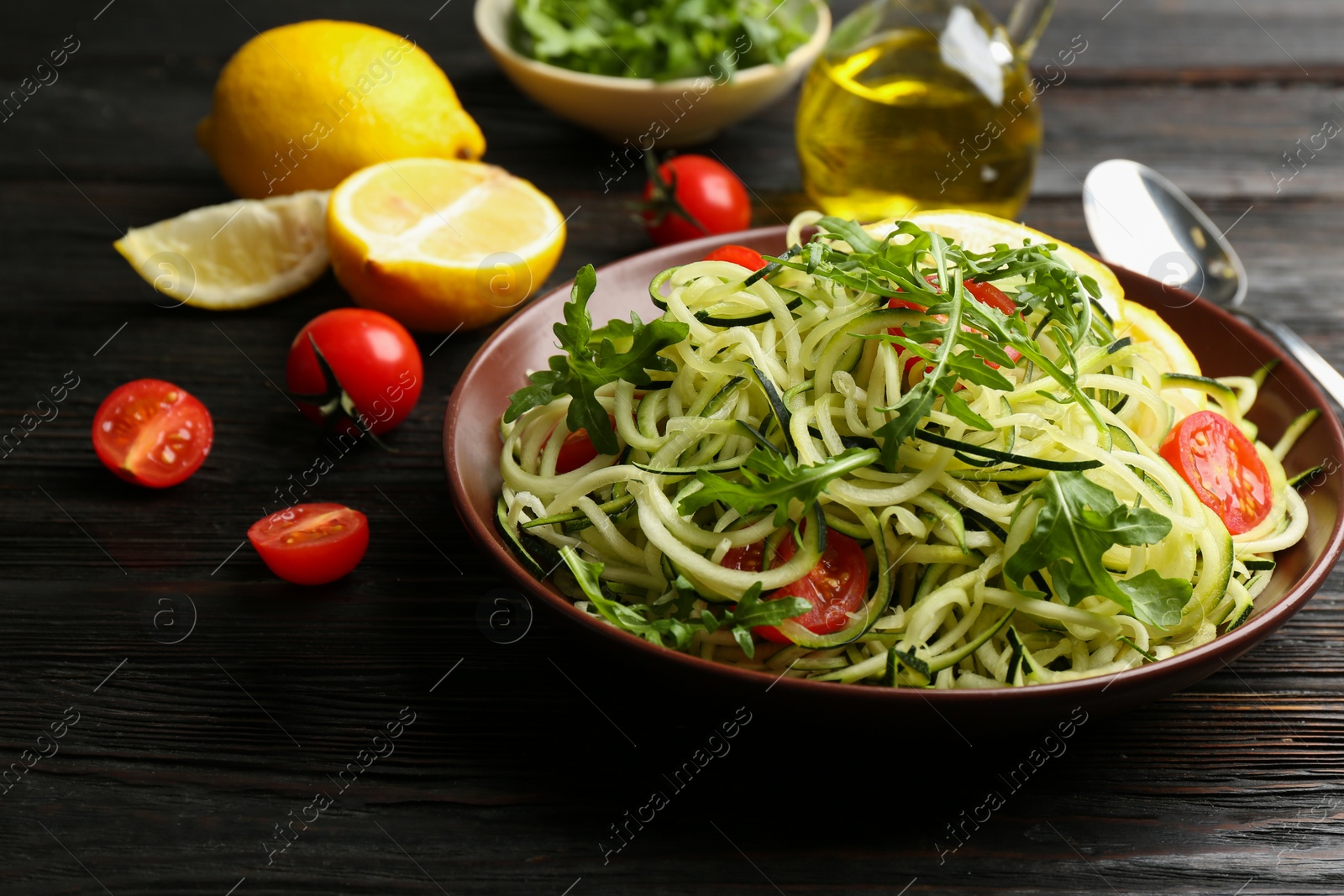Photo of Delicious zucchini pasta with cherry tomatoes and arugula served on black wooden table