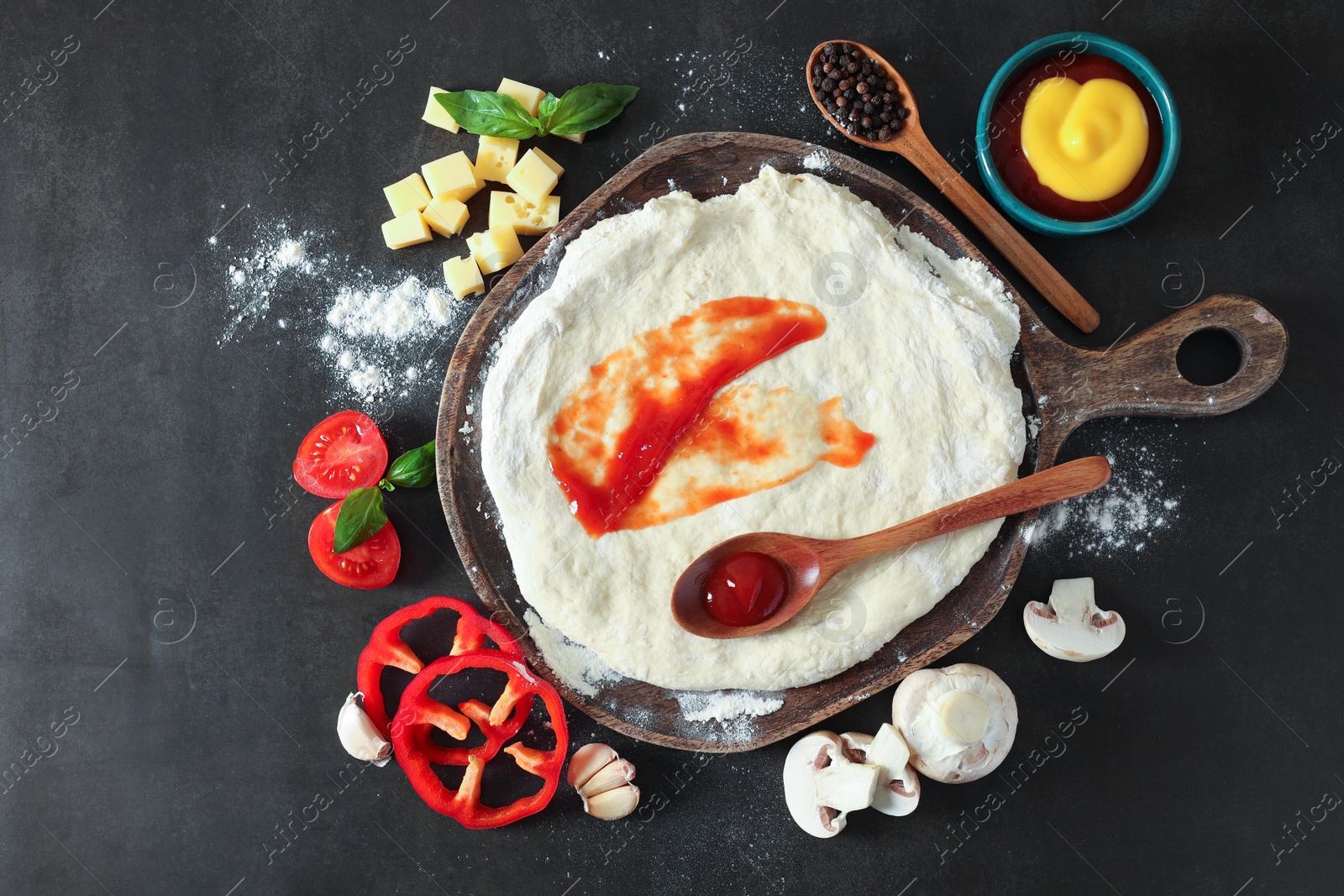 Photo of Pizza dough with tomato sauce and products on dark table, flat lay