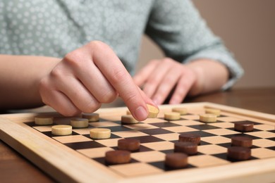 Photo of Playing checkers. Woman thinking about next move at wooden table, closeup