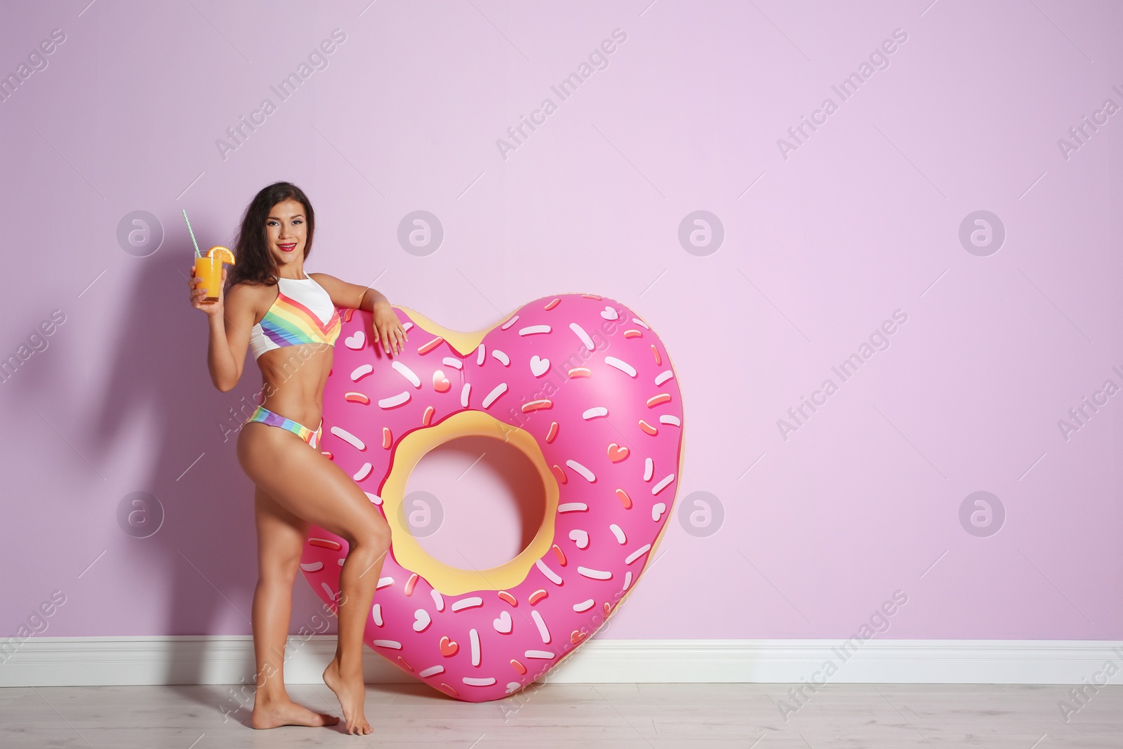 Photo of Beautiful young woman with inflatable heart and glass of cocktail near color wall