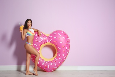 Beautiful young woman with inflatable heart and glass of cocktail near color wall