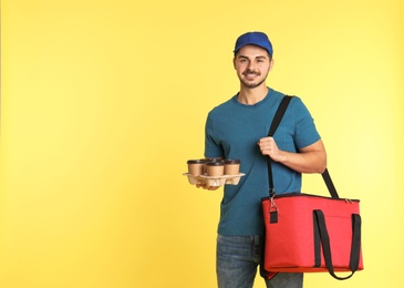 Photo of Young courier with thermo bag and drinks on color background, space for text. Food delivery service