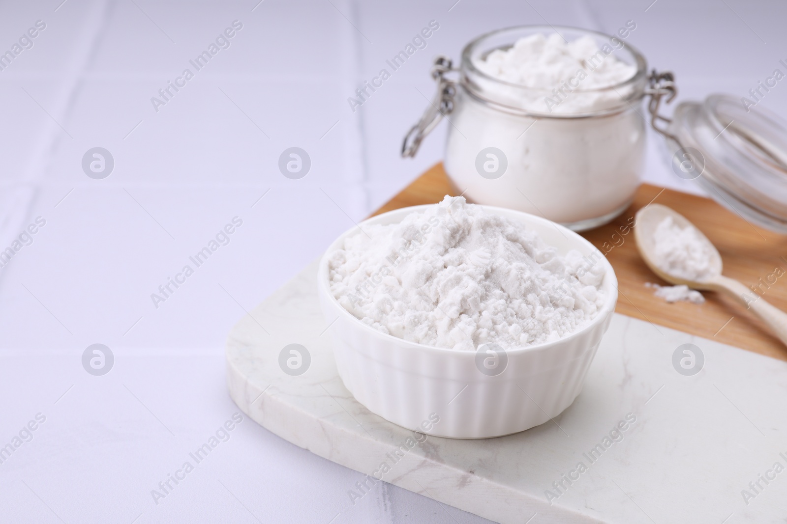 Photo of Bowl, spoon and glass jar of natural starch on white tiled table. Space for text