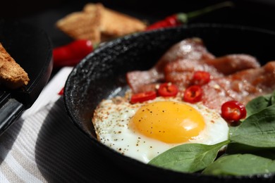 Photo of Tasty fried egg with bacon, chili pepper and spinach on table, closeup