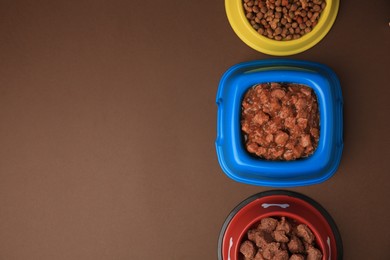 Photo of Dry and wet pet food in feeding bowls on brown background, flat lay. Space for text