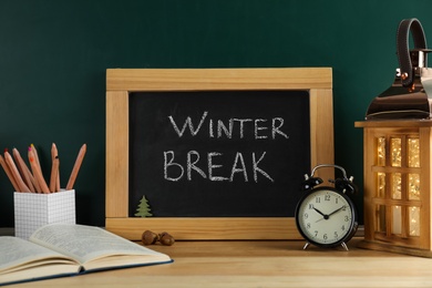 Chalkboard with text Winter Break, alarm clock and school supplies on wooden table. Holidays concept