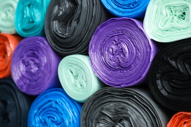 Photo of Rolls of different color garbage bags as background, closeup