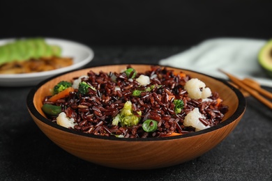 Photo of Plate of brown rice with vegetables on black table, closeup