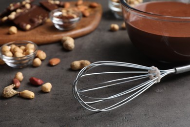 Photo of Whisk, bowl of chocolate cream and nuts on gray table, closeup