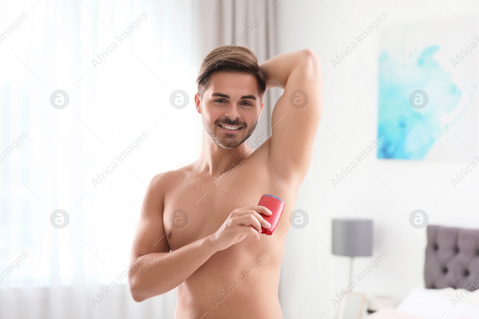 Photo of Handsome young man applying deodorant in bedroom