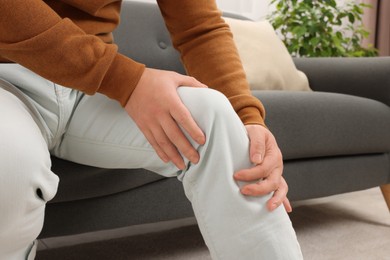 Man suffering from knee pain on sofa indoors, closeup