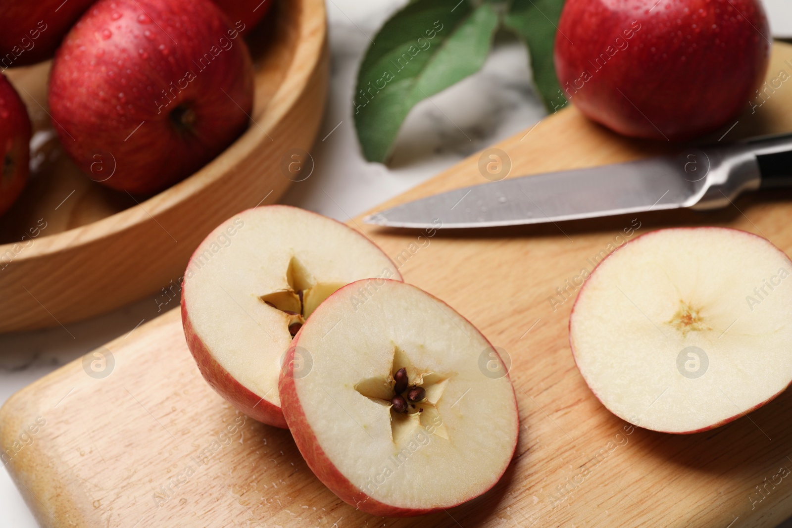 Photo of Cut red apple and knife on white table, closeup