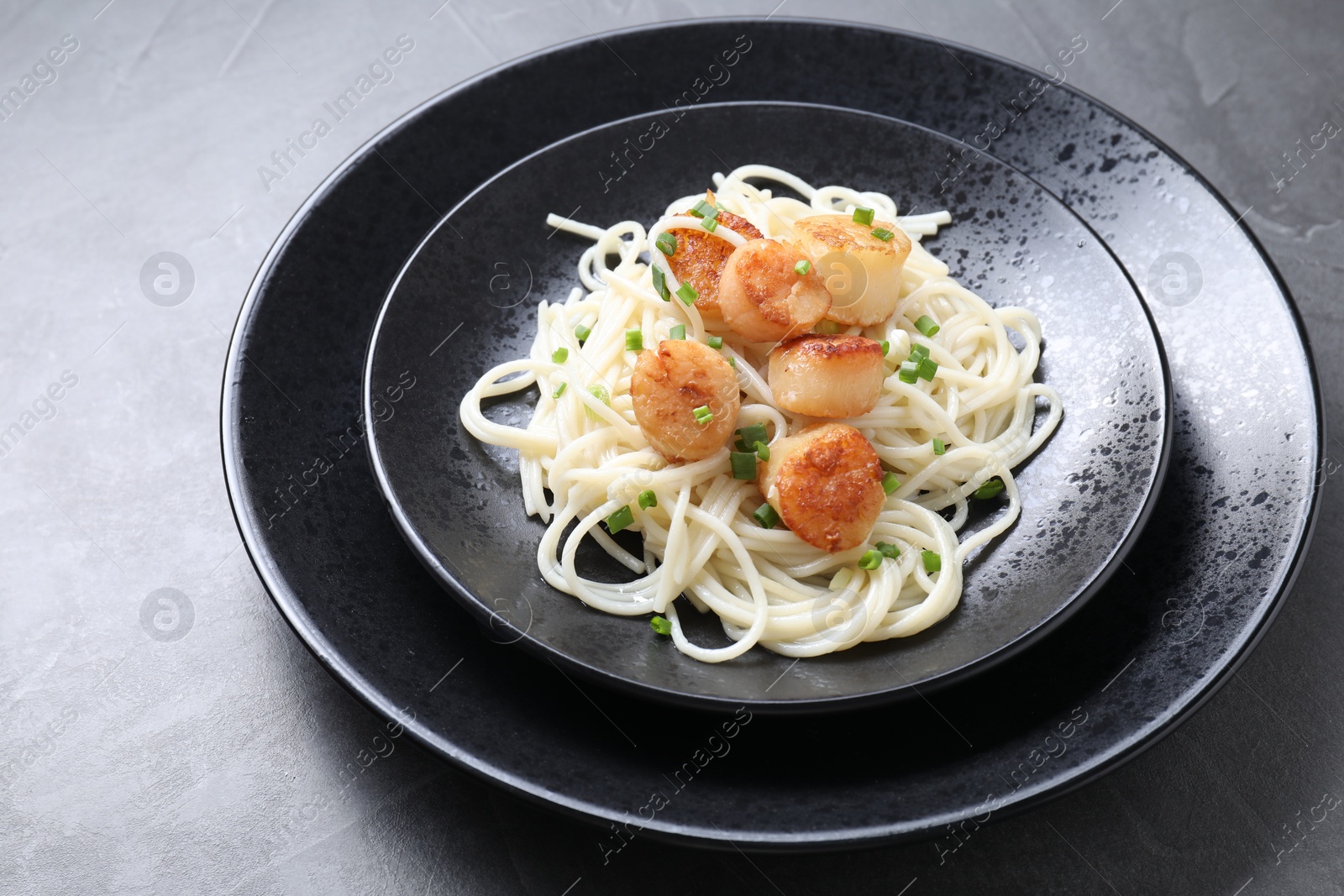 Photo of Delicious scallop pasta with green onion on grey table