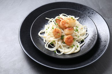 Photo of Delicious scallop pasta with green onion on grey table