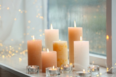 Beautiful burning candles and fairy lights at windowsill on rainy day