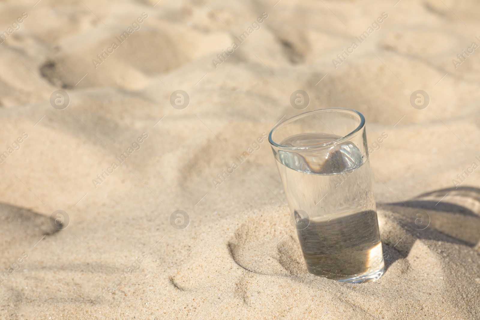 Photo of Sandy beach with glass of refreshing drink on hot summer day, space for text