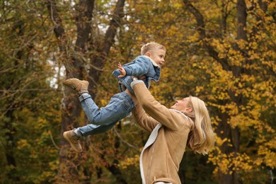 Photo of Happy mother playing with her son in autumn park, low angle view