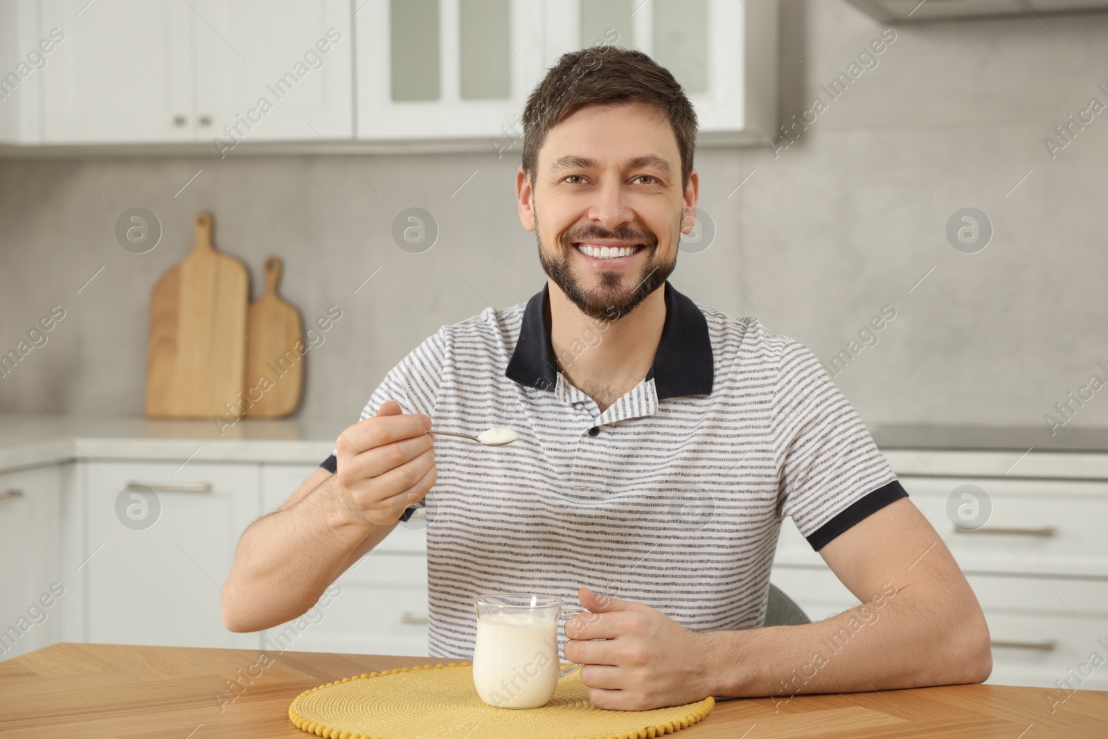 Photo of Handsome man with tasty yogurt at table in kitchen