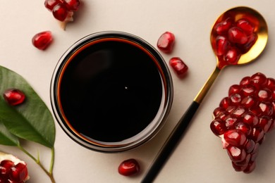 Photo of Glass bowl of tasty pomegranate sauce, fresh ripe fruit and spoon on white background, flat lay