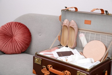 Vintage suitcase with clothes and shoes on sofa indoors