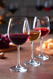 Photo of Glasses with different wines and appetizers on wooden table against blurred background