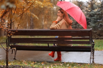 Woman with umbrella sitting on bench in autumn park. Rainy day