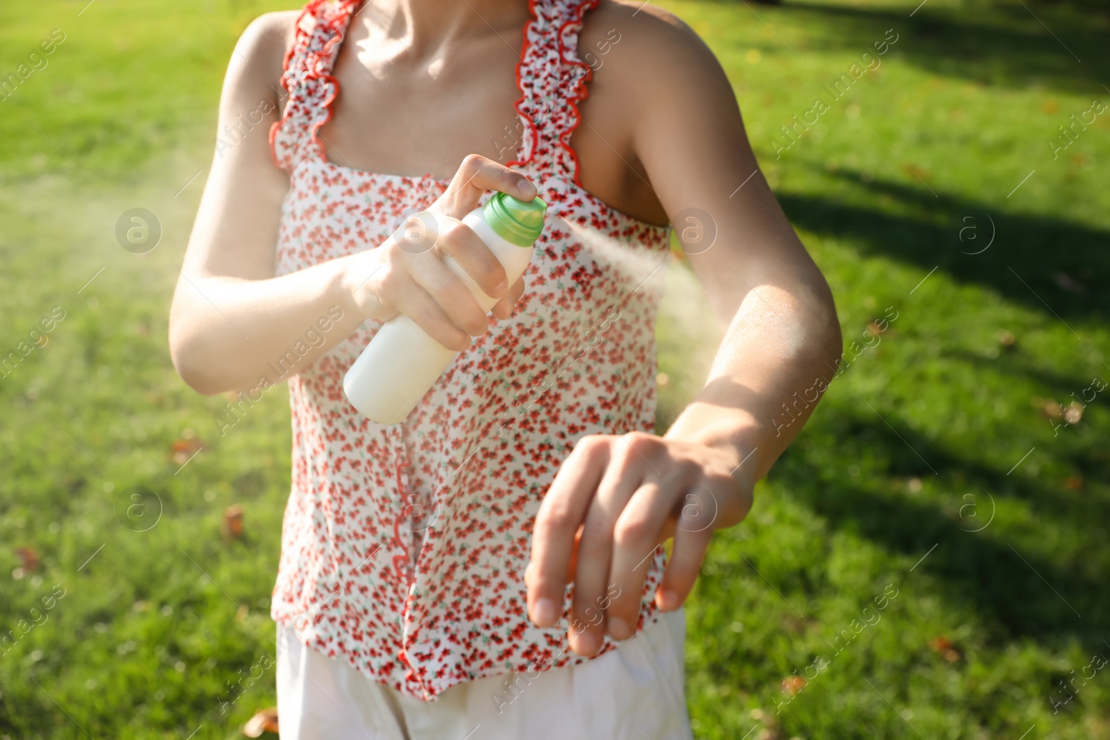 Photo of Woman applying insect repellent onto hand in park, closeup