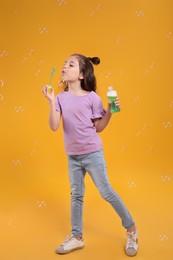 Little girl blowing soap bubbles on yellow background