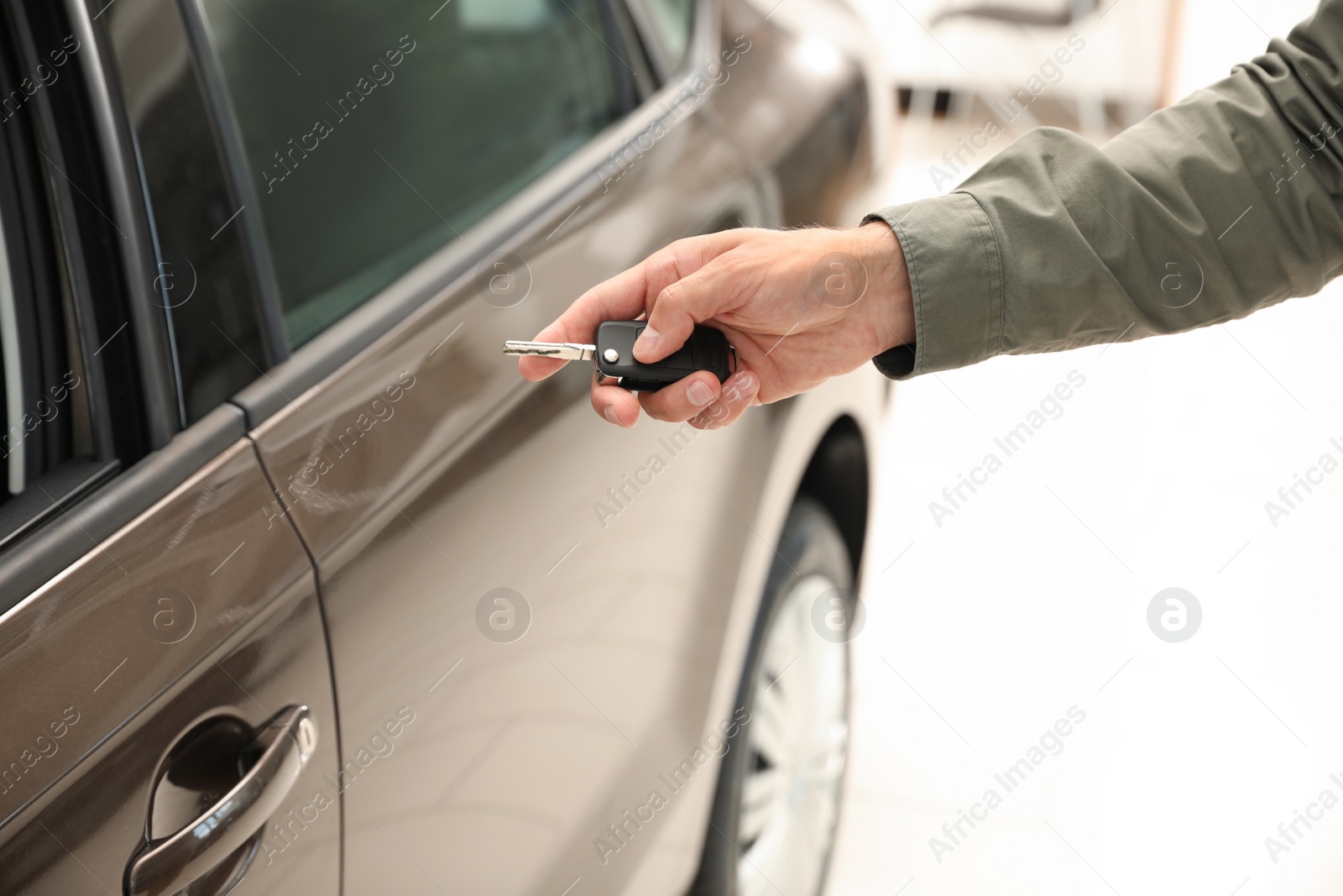 Photo of Young man checking alarm system with car key indoors, closeup