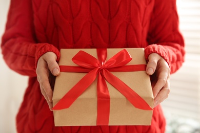 Photo of Woman holding Christmas gift box indoors, closeup