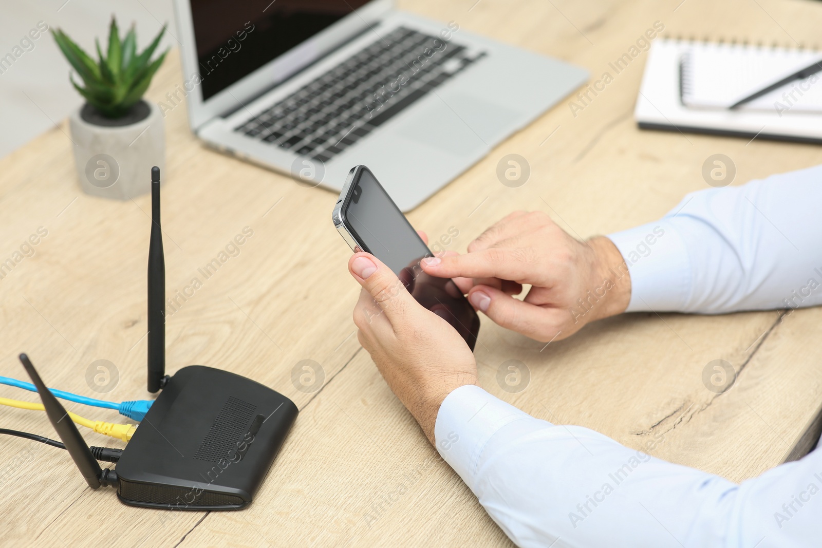 Photo of Man with smartphone and laptop connecting to internet via Wi-Fi router at wooden table, closeup