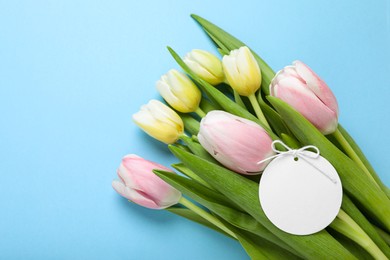 Bouquet of beautiful tulips and blank card on light blue background, top view. Birthday celebration