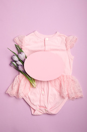 Child's clothes, flowers and card with space for text on pink background, top view