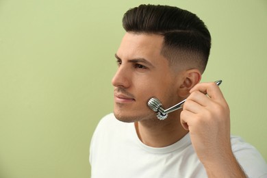 Photo of Man using metal facial roller on green background