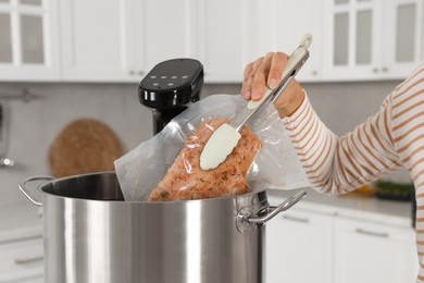 Photo of Woman putting vacuum packed meat into pot with sous vide cooker in kitchen, closeup. Thermal immersion circulator