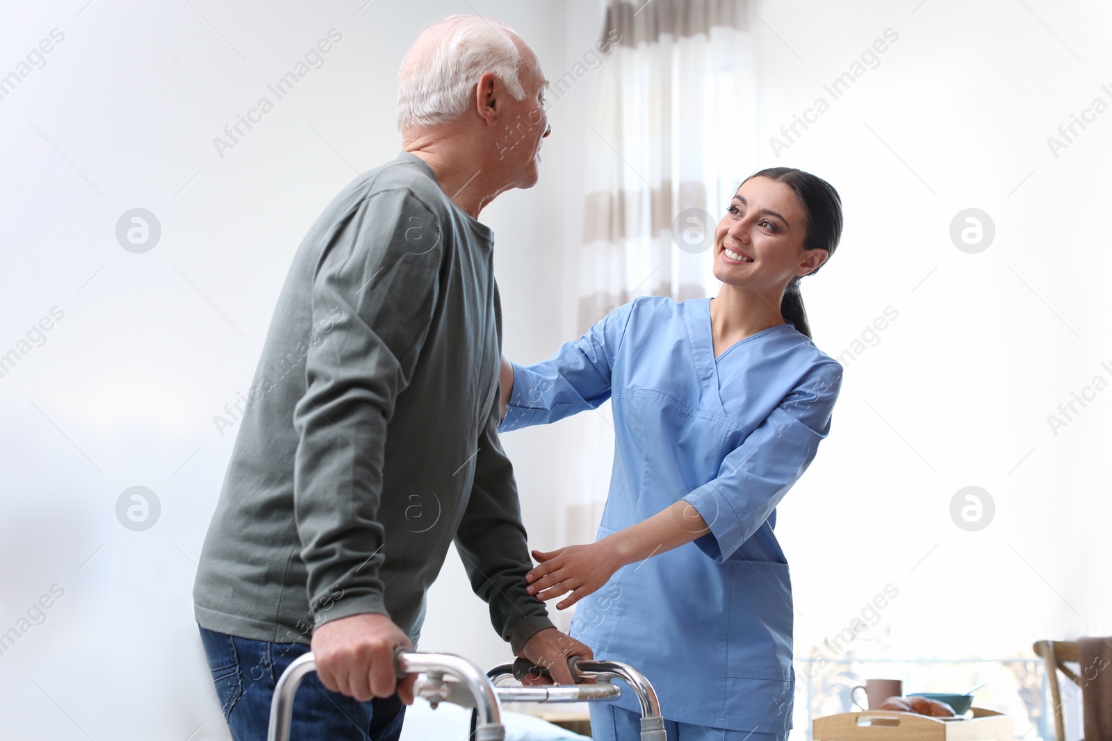 Photo of Care worker helping elderly man with walker in geriatric hospice