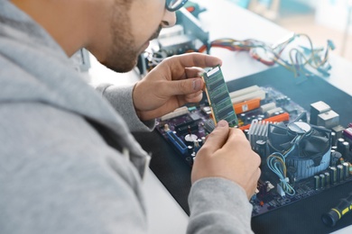 Photo of Male technician repairing motherboard at table, closeup