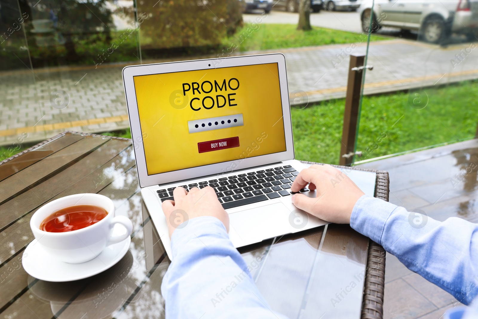 Photo of Man with laptop activating promo code at wooden table outdoors, closeup