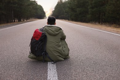 Man with backpack sitting on road near forest, back view