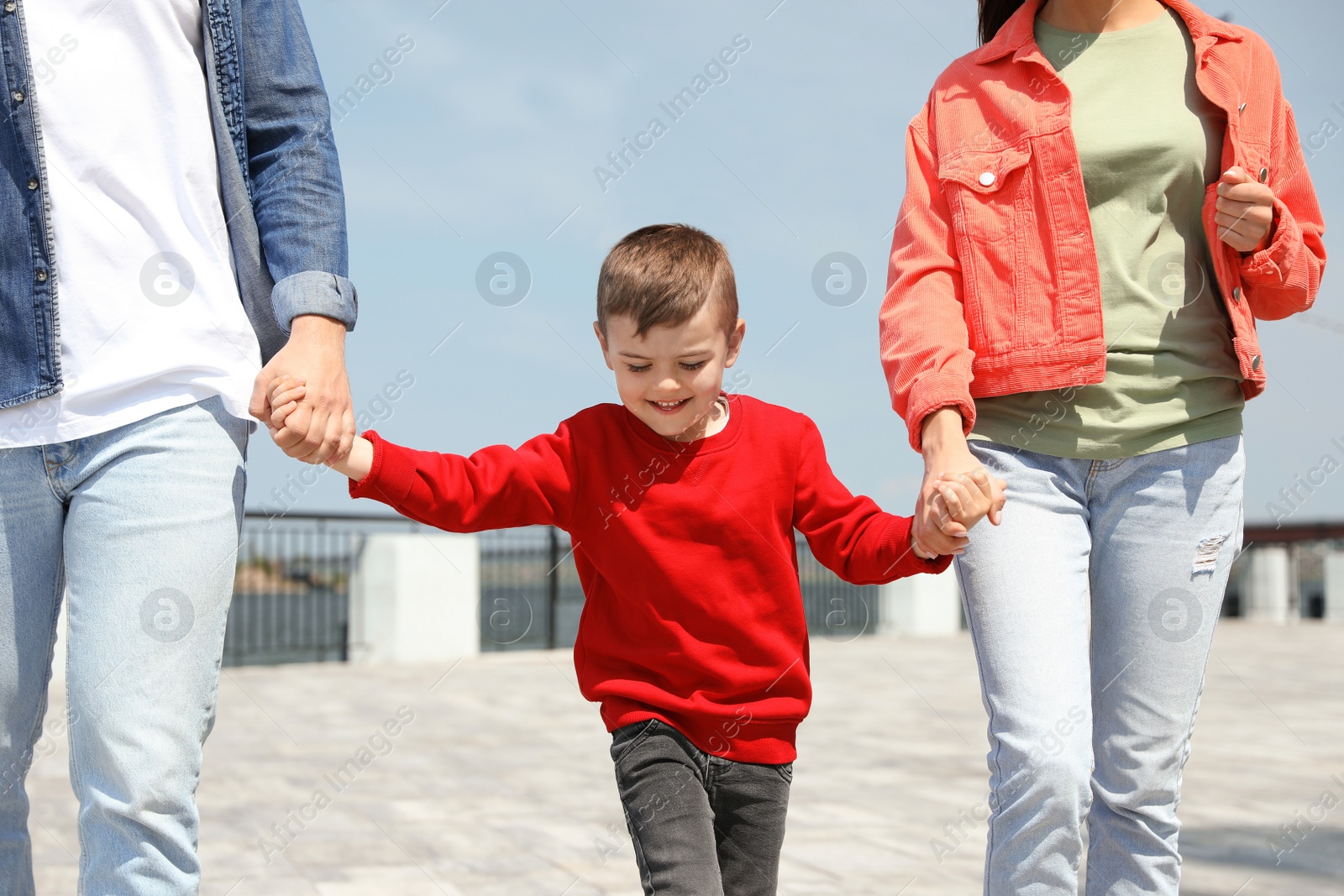 Photo of Happy child holding hands with his parents outdoors. Family weekend