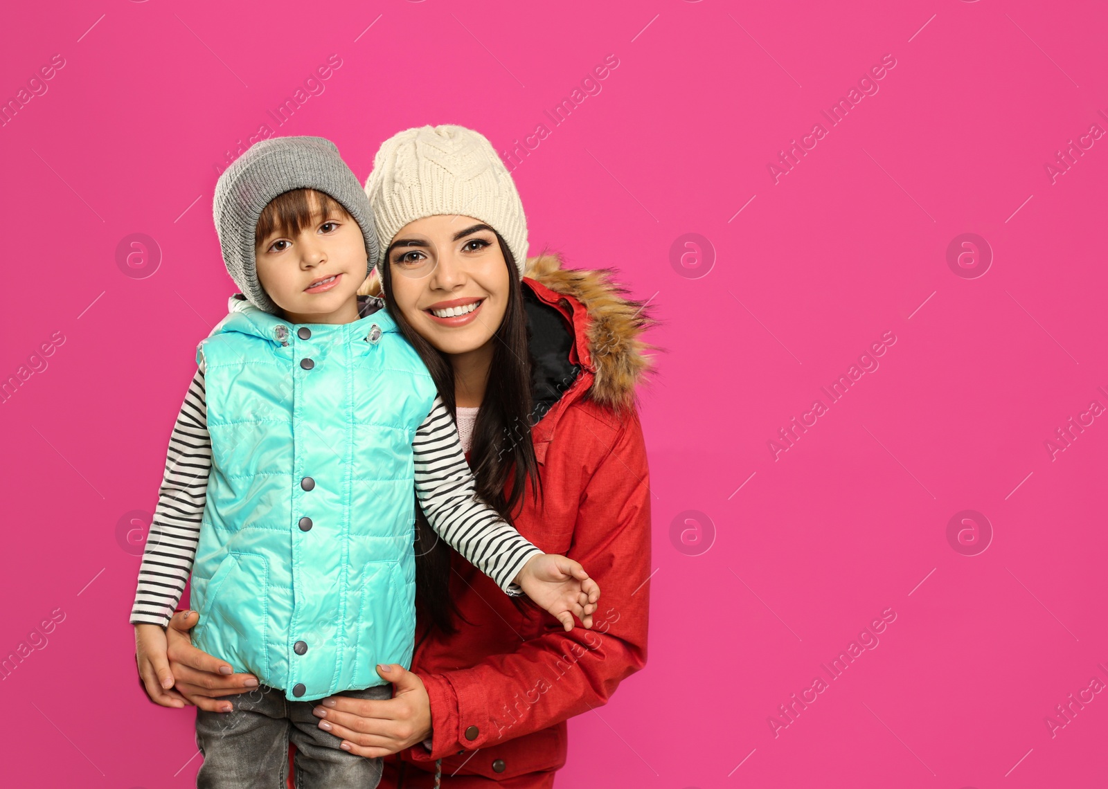 Photo of Happy mother and son in warm clothes on pink background, space for text. Winter vacation