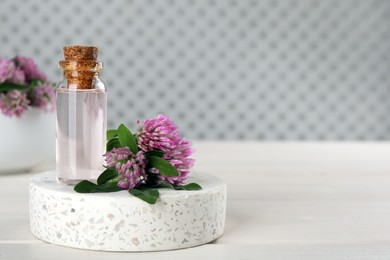 Photo of Beautiful clover flowers and bottle of essential oil on white wooden table. Space for text