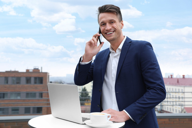 Businessman with laptop talking on phone in outdoor cafe. Corporate blog