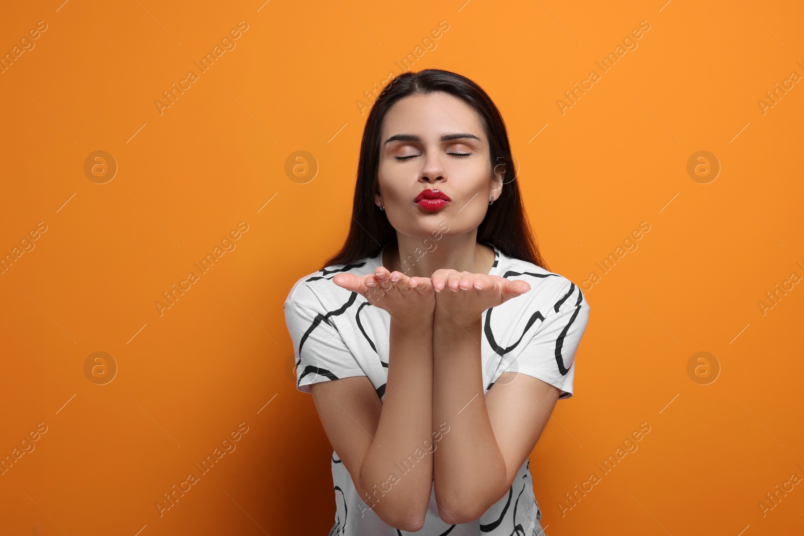 Photo of Beautiful young woman blowing kiss on orange background
