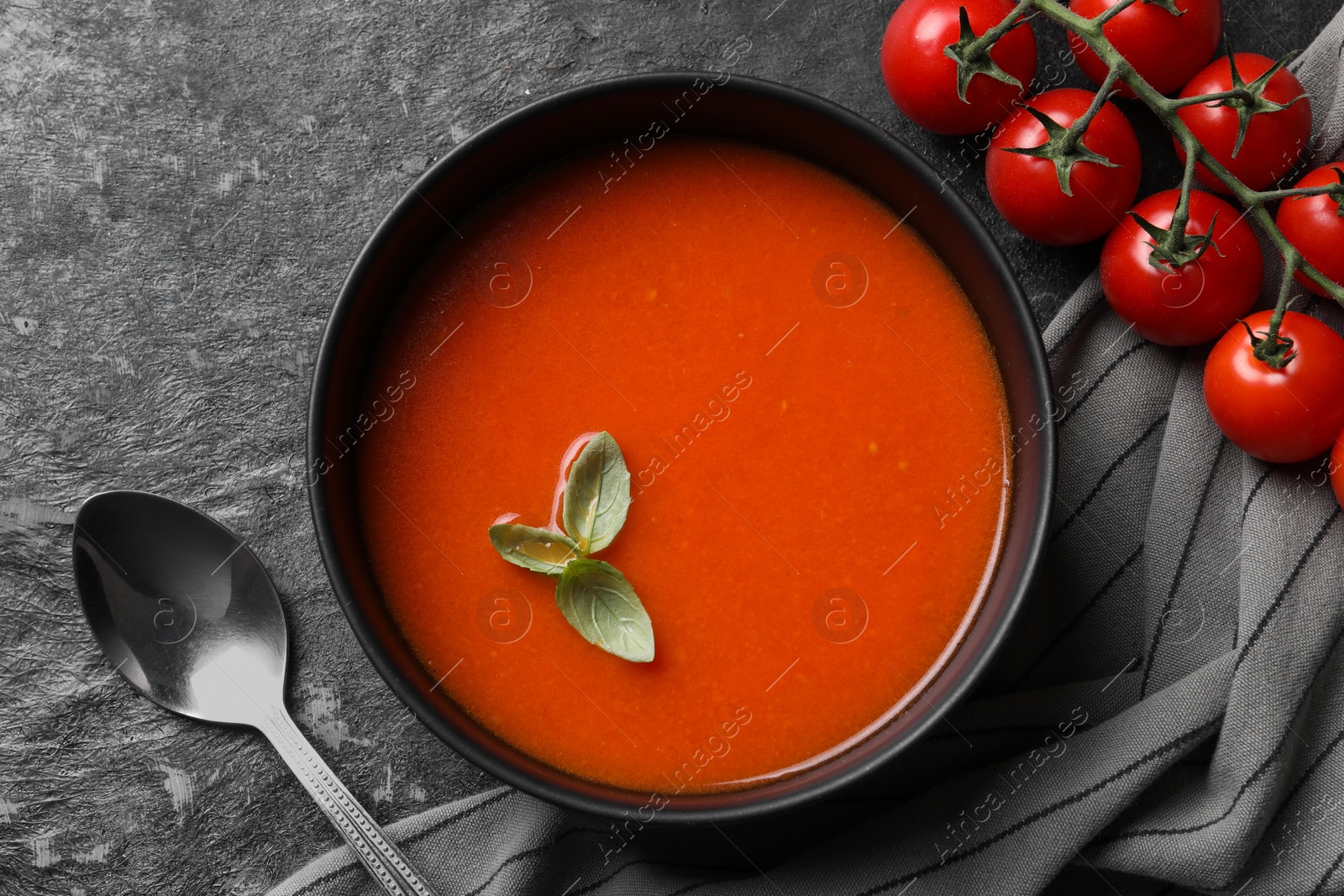 Photo of Delicious tomato cream soup in bowl served on dark textured table, flat lay