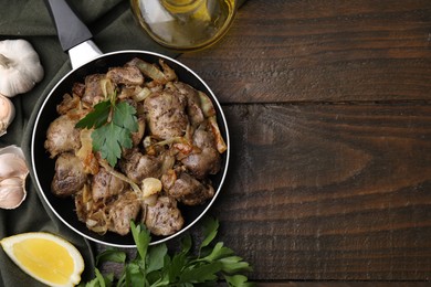 Photo of Tasty fried chicken liver with onion and parsley served on wooden table, flat lay. Space for text